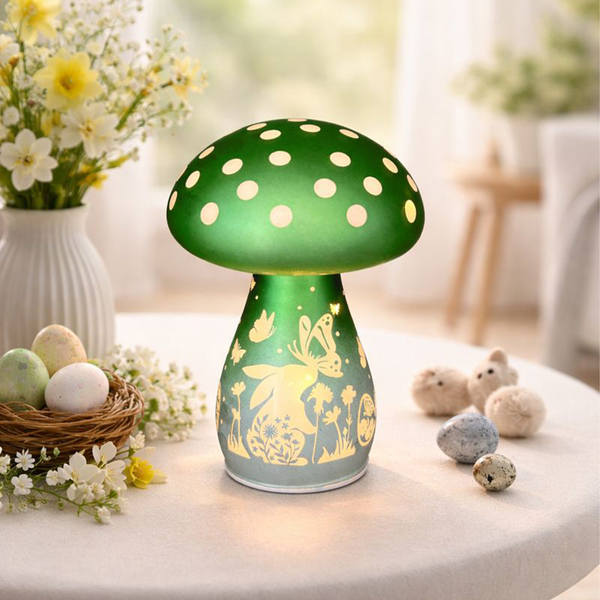 Grüne Pilzlampe mit Punkten auf einem Tisch, umgeben von Blumen und dekorativen Eiern.